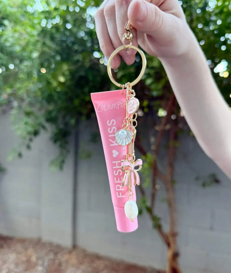 Hand holding pink Fresh Kiss lip tube keychain