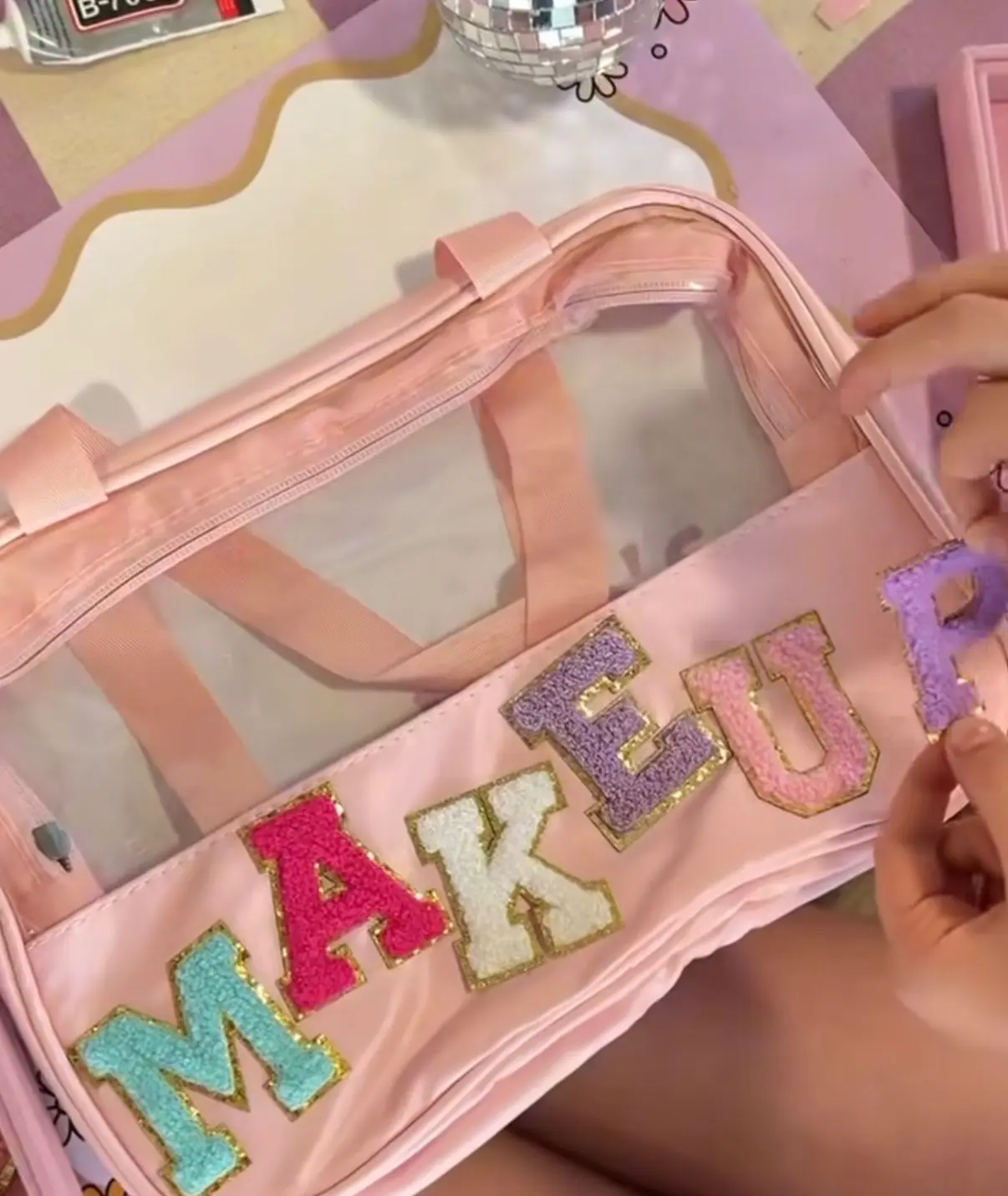 Hands placing glitter "MAKEUP" letters on pink bag