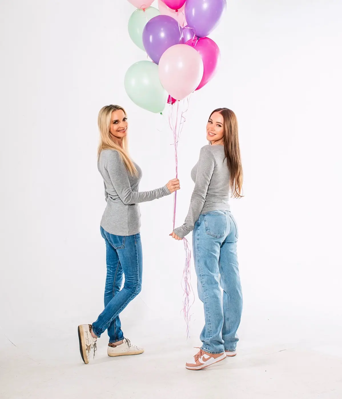 Two women in jeans holding pastel balloons