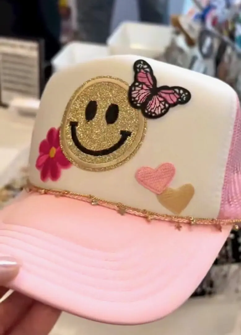 White and pink cap with smiley face, butterfly, and hearts.