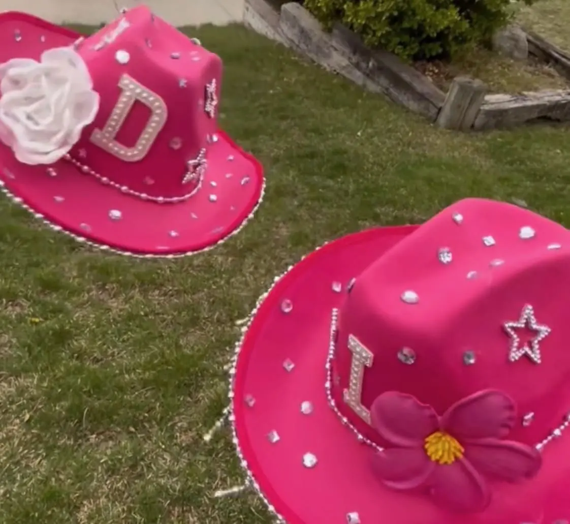 Two decorated pink cowboy hats placed on grass outdoors.