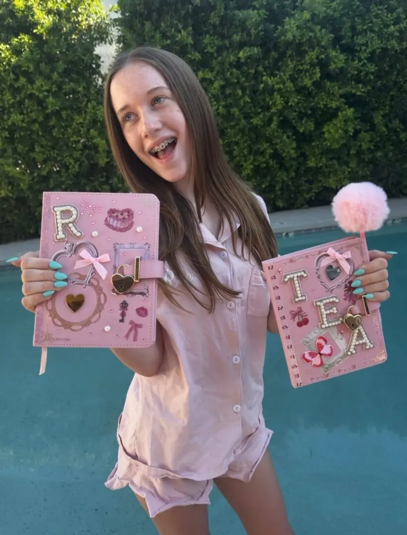 Smiling girl holding decorated pink journals by pool