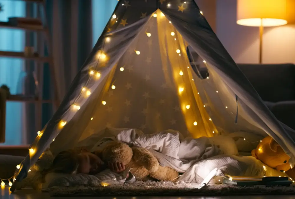 Child sleeping in tent with fairy lights.